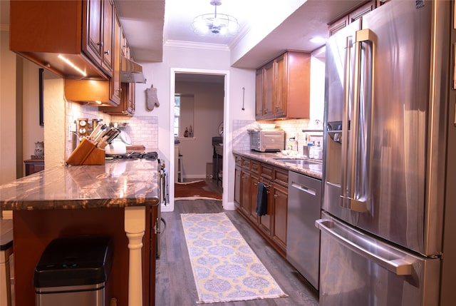 kitchen featuring dark hardwood / wood-style floors, tasteful backsplash, appliances with stainless steel finishes, crown molding, and dark stone countertops