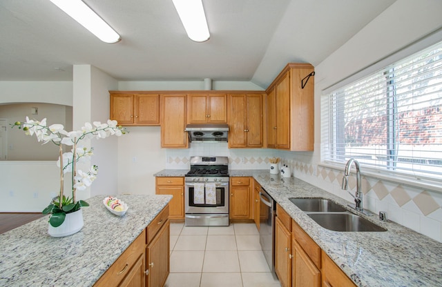 kitchen featuring stainless steel appliances, light stone counters, exhaust hood, and sink