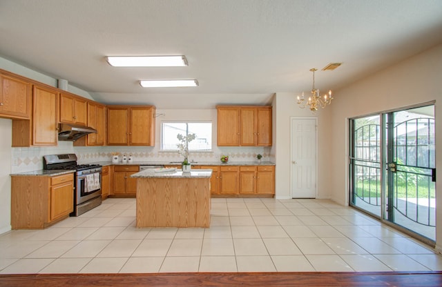 kitchen featuring gas stove, light stone counters, a center island, tasteful backsplash, and an inviting chandelier