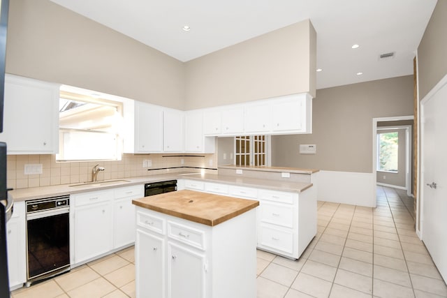 kitchen with light tile patterned flooring, sink, kitchen peninsula, a kitchen island, and white cabinets