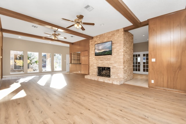 unfurnished living room featuring ceiling fan, light hardwood / wood-style floors, beamed ceiling, and a fireplace