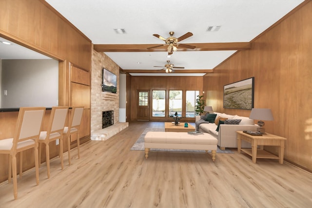 living room featuring a brick fireplace, wood walls, ceiling fan, beam ceiling, and light wood-type flooring