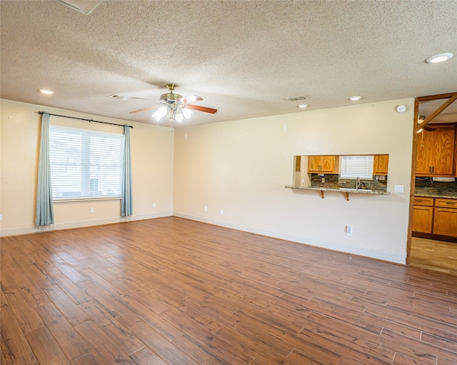 unfurnished living room featuring a textured ceiling, light hardwood / wood-style floors, sink, and ceiling fan