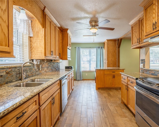 kitchen with decorative backsplash, light hardwood / wood-style floors, light stone countertops, stainless steel appliances, and sink