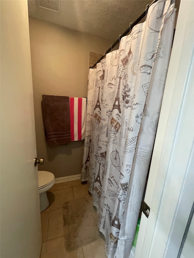 bathroom featuring toilet, a textured ceiling, walk in shower, and tile patterned flooring