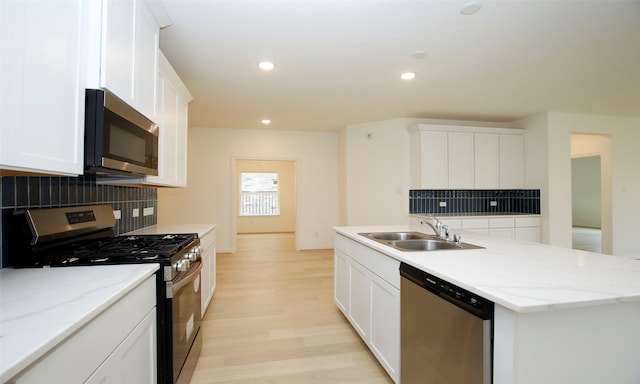 kitchen with decorative backsplash, stainless steel appliances, sink, white cabinetry, and an island with sink