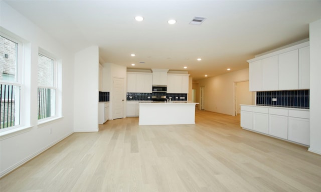 kitchen featuring light wood-type flooring, tasteful backsplash, stainless steel appliances, a kitchen island with sink, and white cabinets