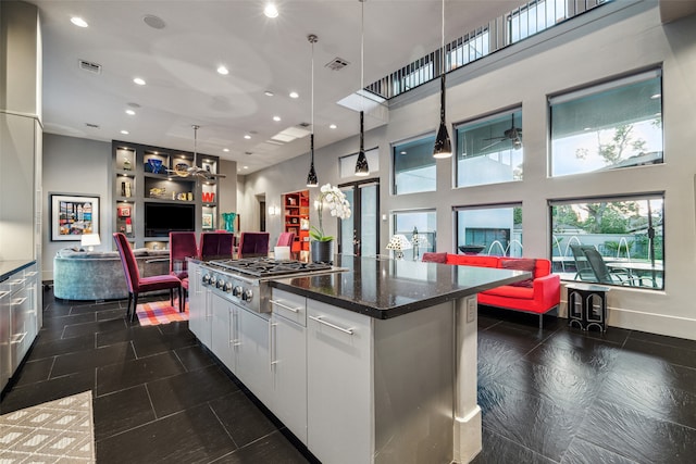 kitchen featuring a high ceiling, pendant lighting, dark stone countertops, stainless steel gas stovetop, and white cabinetry