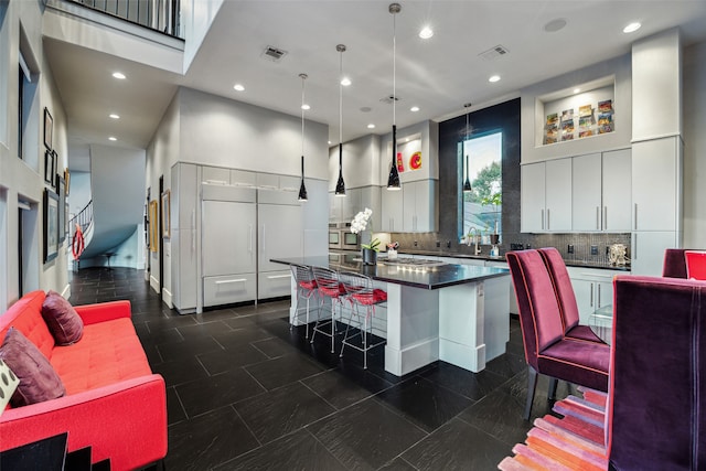 kitchen with pendant lighting, a kitchen island, a breakfast bar area, decorative backsplash, and white cabinetry