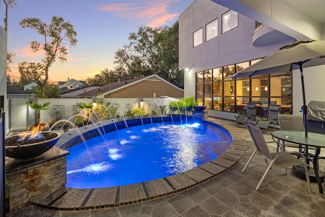 pool at dusk featuring an outdoor fire pit, a patio, and pool water feature