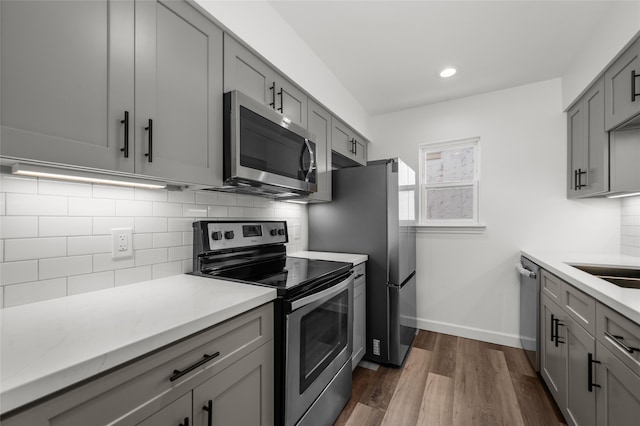 kitchen featuring gray cabinetry, stainless steel appliances, backsplash, and dark wood-type flooring