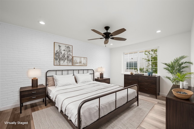 bedroom with light wood-type flooring, ceiling fan, and brick wall