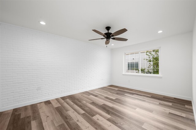 empty room with light hardwood / wood-style flooring, ceiling fan, and brick wall