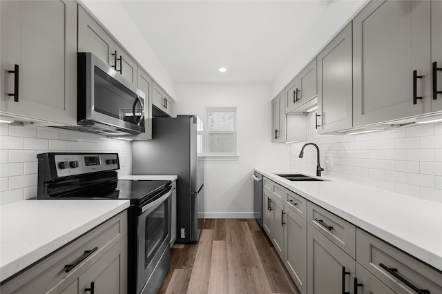 kitchen with gray cabinets, tasteful backsplash, dark wood-type flooring, sink, and stainless steel appliances