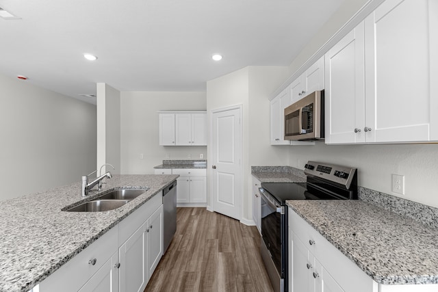 kitchen with light stone counters, appliances with stainless steel finishes, white cabinetry, light hardwood / wood-style floors, and sink