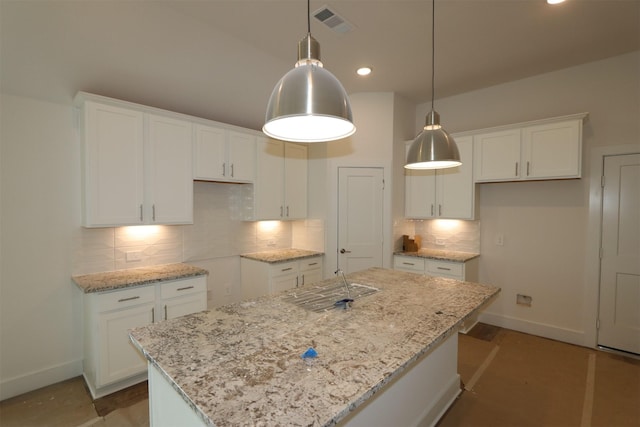 kitchen with hanging light fixtures, light stone counters, a kitchen island, and white cabinets