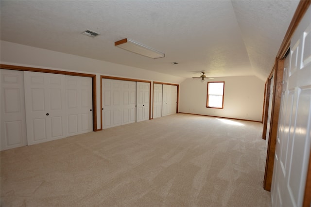 spare room with a textured ceiling, lofted ceiling, ceiling fan, and light carpet