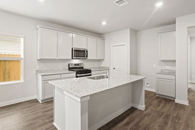 kitchen with appliances with stainless steel finishes, sink, white cabinetry, light stone counters, and a center island with sink