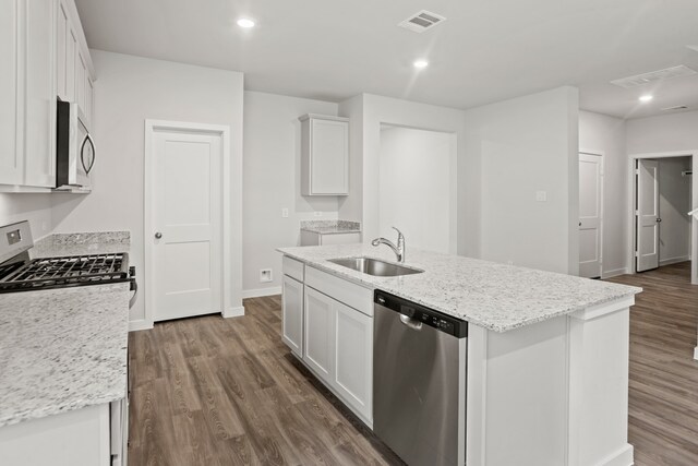 kitchen with light stone countertops, white cabinets, appliances with stainless steel finishes, sink, and a kitchen island with sink