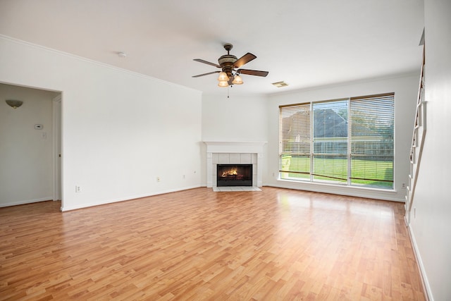 unfurnished living room featuring ornamental molding, light hardwood / wood-style floors, ceiling fan, and a tiled fireplace