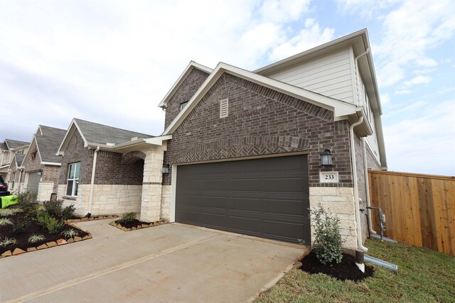 view of property exterior featuring fence, driveway, an attached garage, stone siding, and brick siding