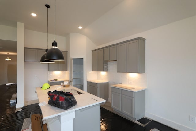 kitchen featuring an island with sink, gray cabinetry, decorative backsplash, vaulted ceiling, and hanging light fixtures