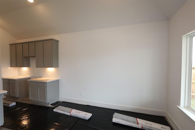 kitchen featuring decorative backsplash, lofted ceiling, baseboards, and gray cabinetry