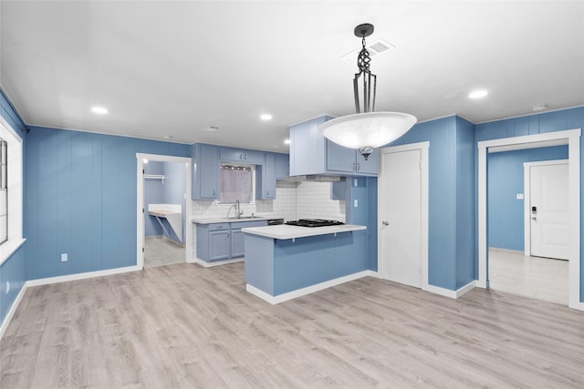 kitchen featuring stainless steel gas stovetop, sink, decorative light fixtures, light hardwood / wood-style floors, and kitchen peninsula