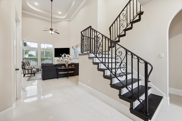 stairs featuring a towering ceiling, a tray ceiling, ceiling fan, and tile patterned floors