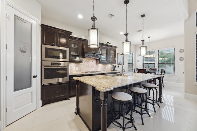 kitchen with hanging light fixtures, sink, dark brown cabinets, a kitchen island with sink, and appliances with stainless steel finishes