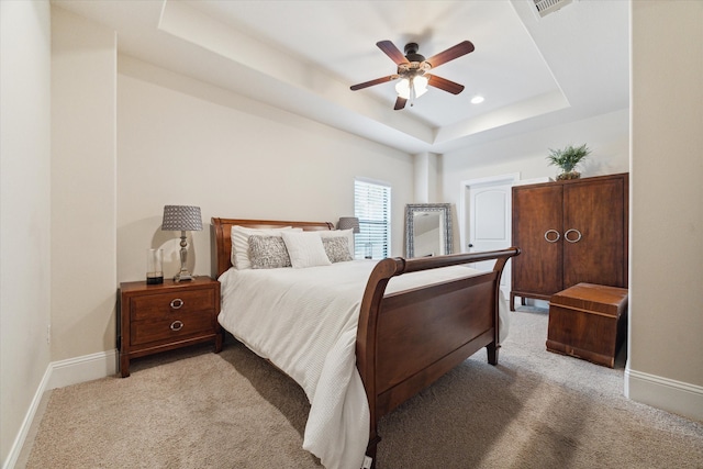 bedroom with ceiling fan, light colored carpet, and a tray ceiling