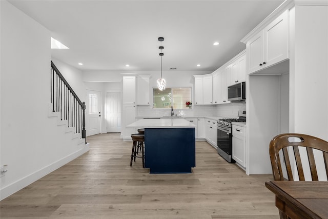 kitchen with a kitchen island, a kitchen breakfast bar, white cabinetry, stainless steel appliances, and light hardwood / wood-style flooring