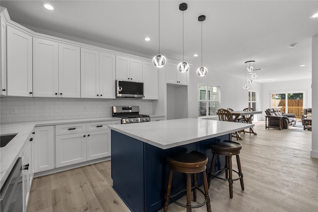 kitchen featuring white cabinets, hanging light fixtures, a kitchen island, light hardwood / wood-style flooring, and stainless steel appliances