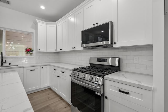 kitchen with light hardwood / wood-style floors, white cabinetry, stainless steel appliances, and light stone counters