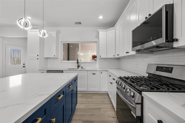 kitchen featuring hanging light fixtures, white cabinetry, blue cabinets, appliances with stainless steel finishes, and light stone counters