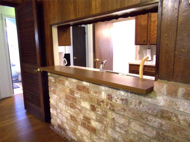 kitchen with brick wall, sink, wood walls, and dark wood-type flooring