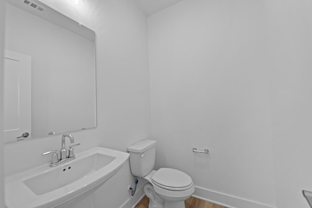 half bathroom featuring wood finished floors, visible vents, toilet, a sink, and baseboards