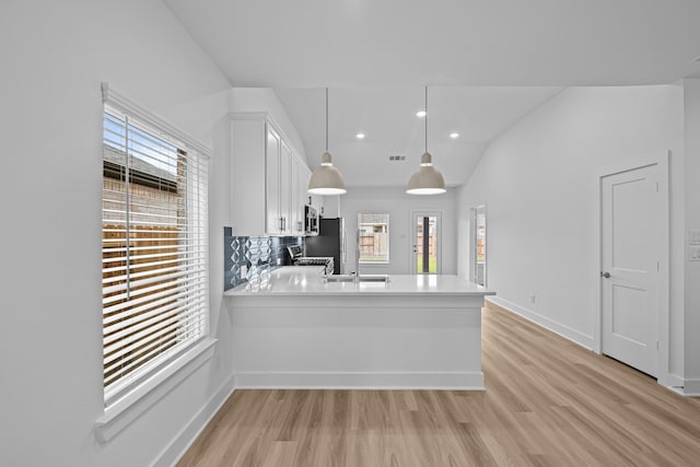 kitchen featuring white cabinets, light wood finished floors, light countertops, decorative light fixtures, and a peninsula