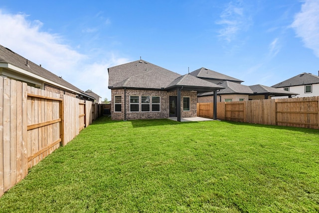 back of property with brick siding, a patio area, a lawn, a fenced backyard, and roof with shingles