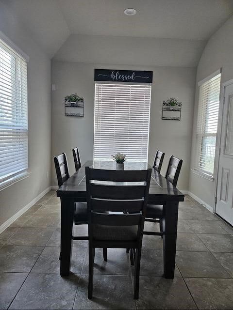 dining space featuring dark tile patterned flooring, vaulted ceiling, and a healthy amount of sunlight