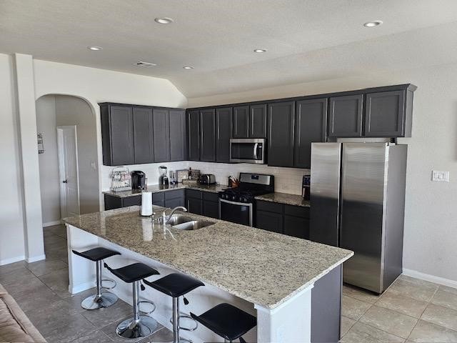 kitchen with light stone counters, sink, an island with sink, and appliances with stainless steel finishes