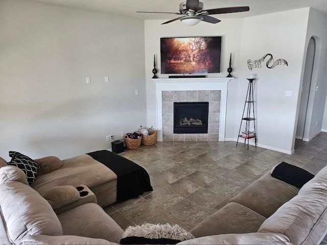 living room featuring ceiling fan and a tiled fireplace