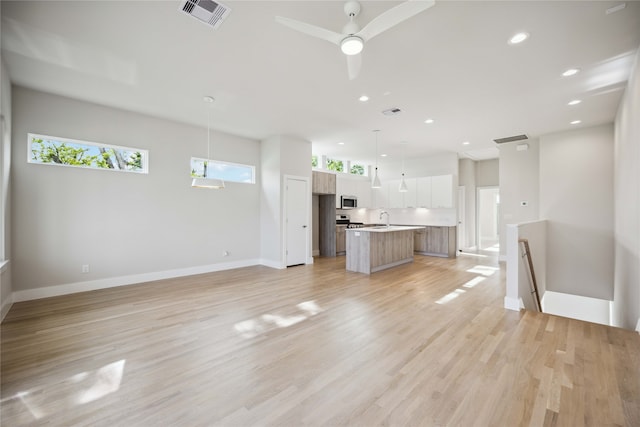 unfurnished living room with light wood-type flooring, sink, ceiling fan, and a wealth of natural light