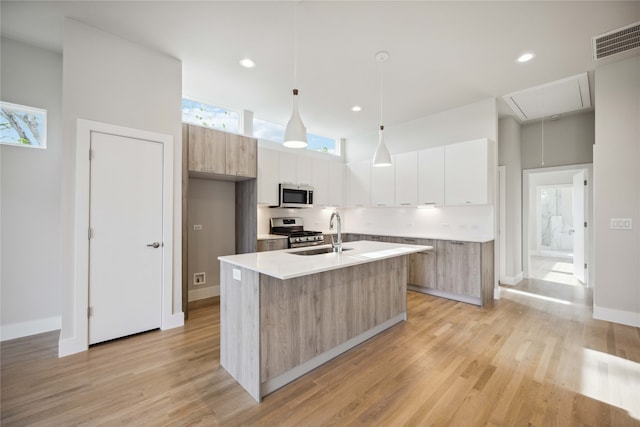 kitchen with pendant lighting, an island with sink, sink, white cabinetry, and stainless steel appliances