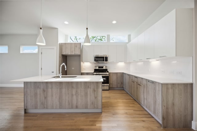 kitchen featuring an island with sink, stainless steel appliances, white cabinetry, and hanging light fixtures