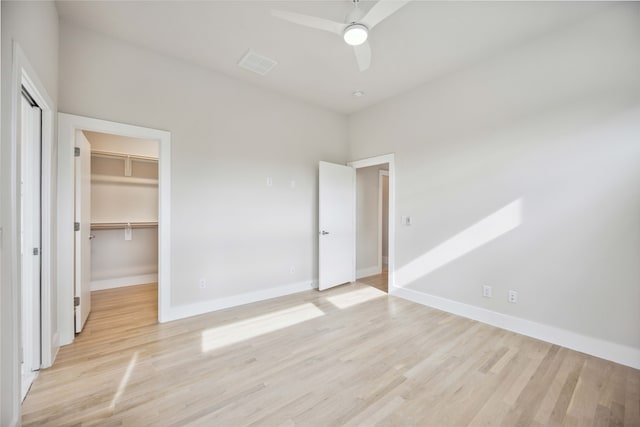 unfurnished bedroom with light hardwood / wood-style flooring, a closet, ceiling fan, and a walk in closet