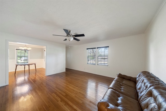 unfurnished living room with ceiling fan with notable chandelier, dark hardwood / wood-style floors, crown molding, and a healthy amount of sunlight