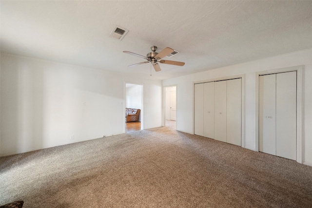 unfurnished bedroom featuring multiple closets, carpet, and ceiling fan