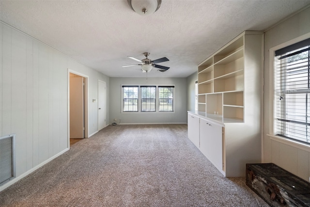 carpeted empty room with ceiling fan, a textured ceiling, and wooden walls