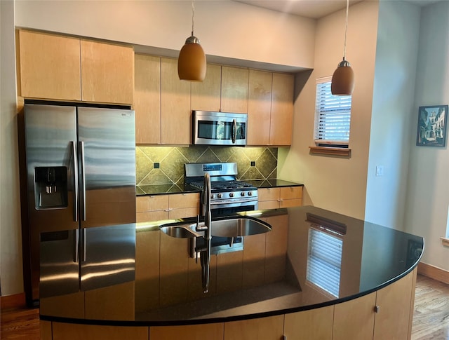 kitchen with light brown cabinets, decorative light fixtures, backsplash, stainless steel appliances, and light wood-type flooring